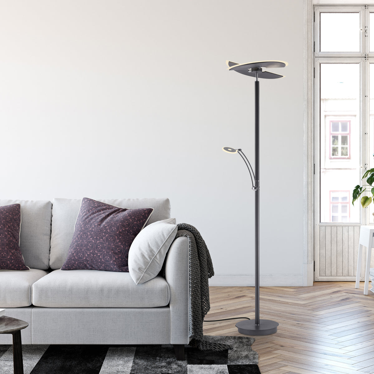 Lampadaire allumé dans un salon près d'un canapé gris et d'une fenêtre.