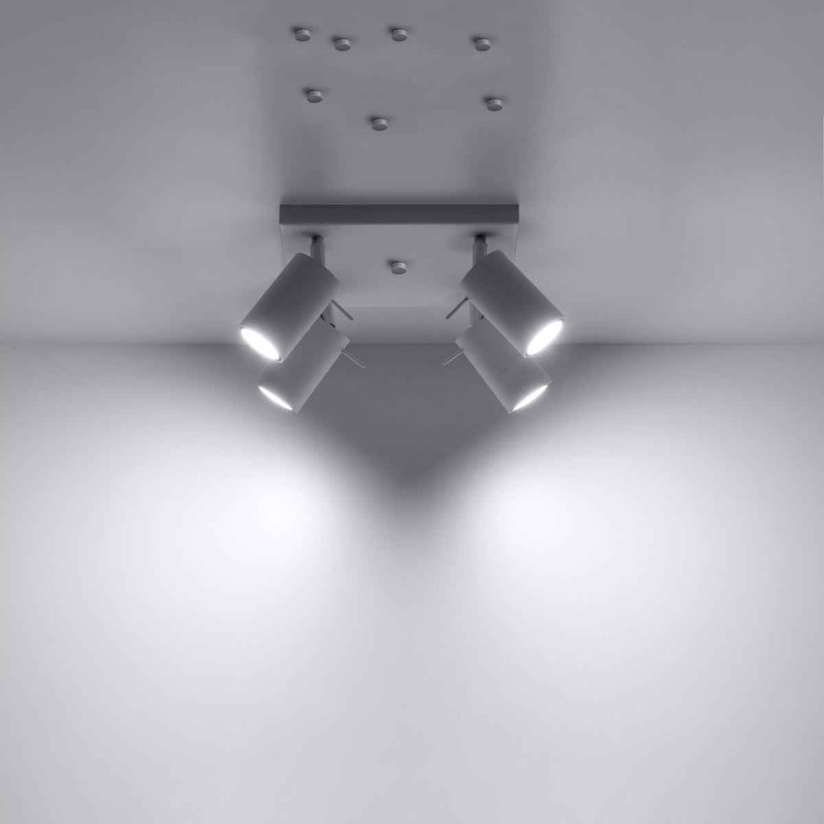 Plafonnier allumé projetant quatre faisceaux lumineux sur un mur clair