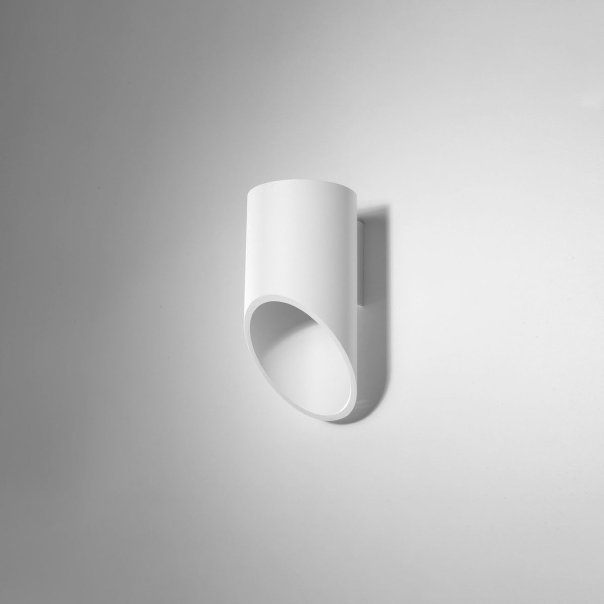 Applique cylindrique blanche photographiée de face contre un mur blanc, ombre portée douce.