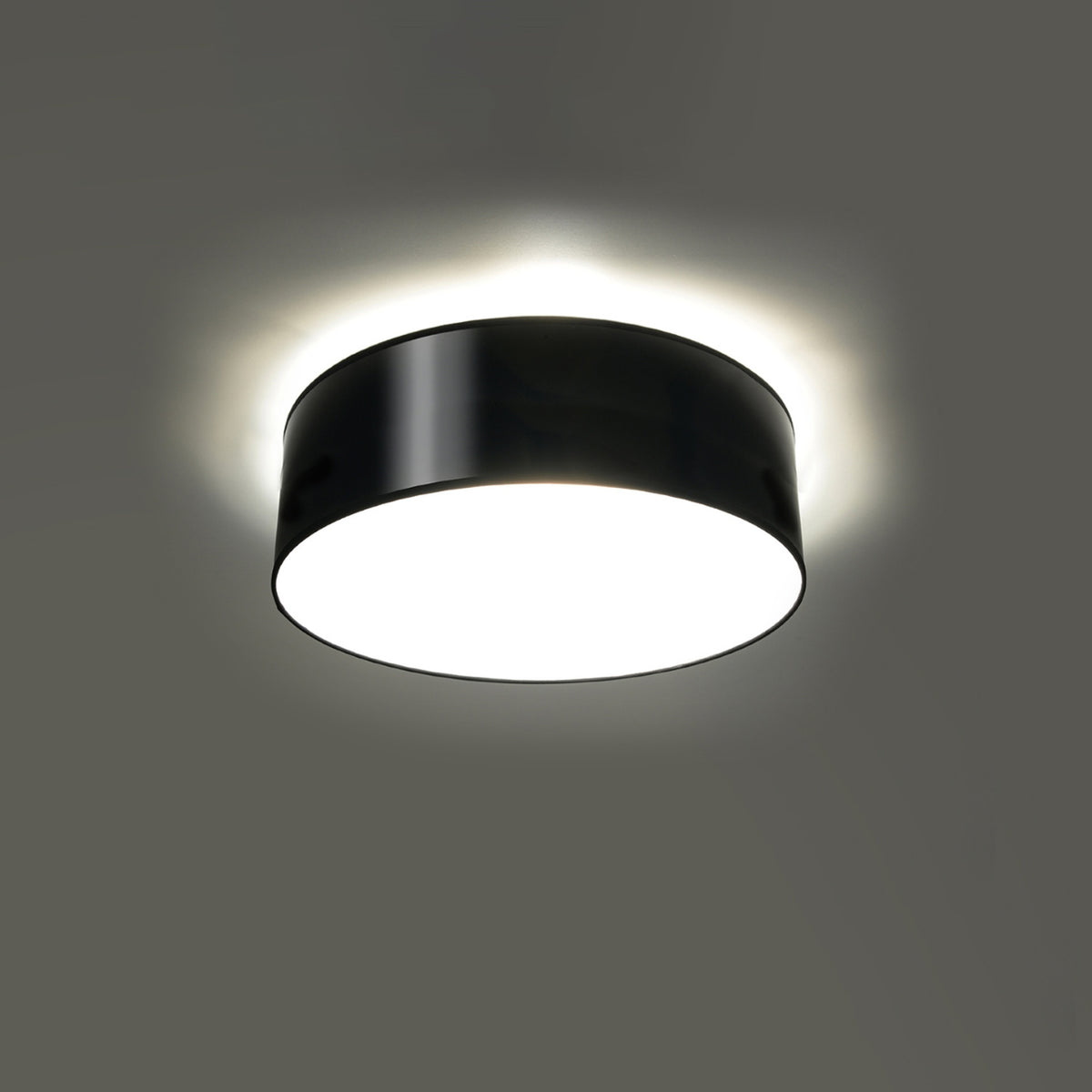Plafonnier allumé au plafond, halo lumineux diffus autour du cylindre noir brillant