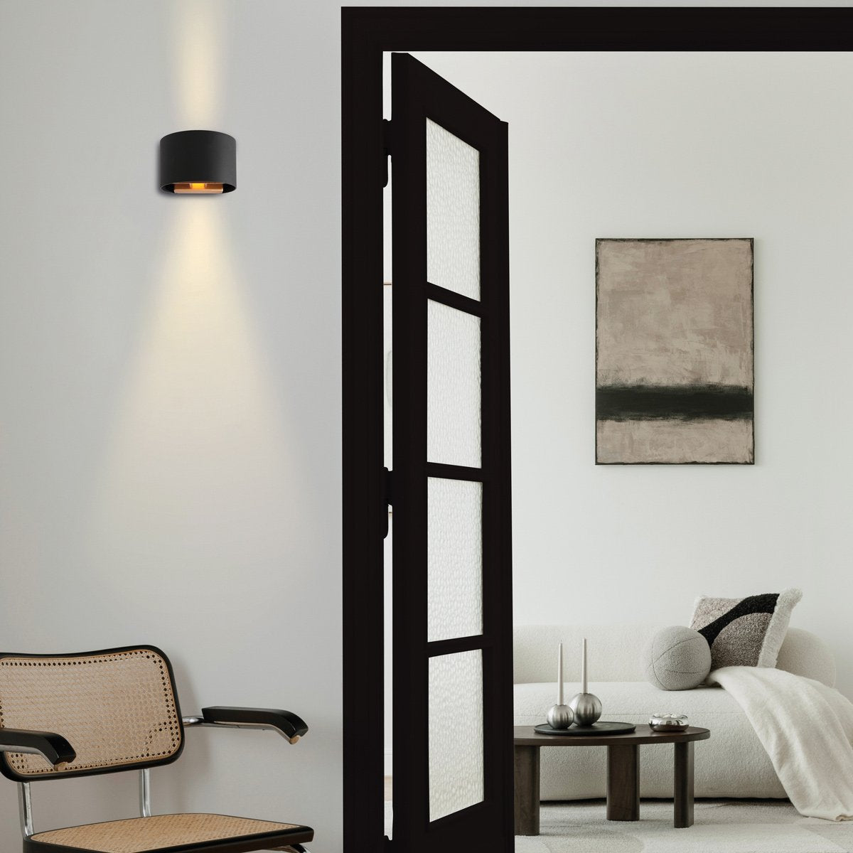 Ambiance intérieure épurée, applique murale noire allumée près d'une porte noire.