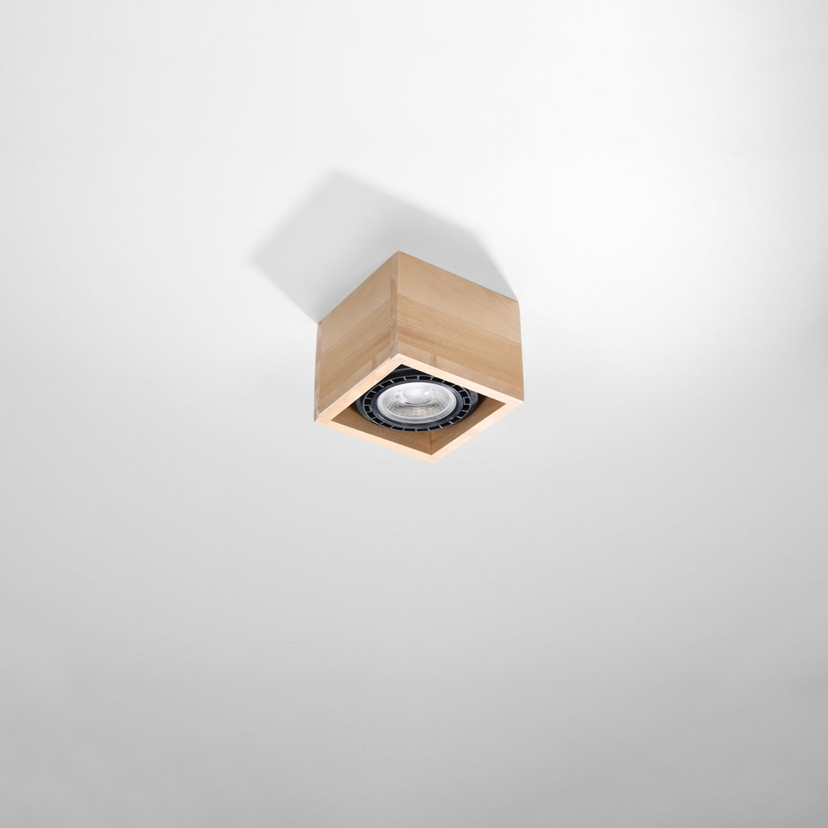 Plafonnier carré en bois installé seul au plafond blanc, vue légèrement en contre-plongée.
