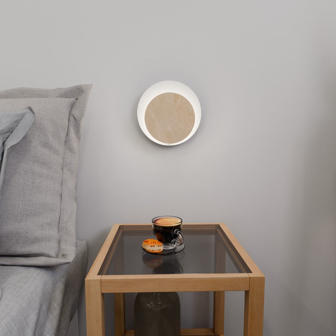 Vue frontale allumée sur mur gris, anneau lumineux entourant la face en bois.