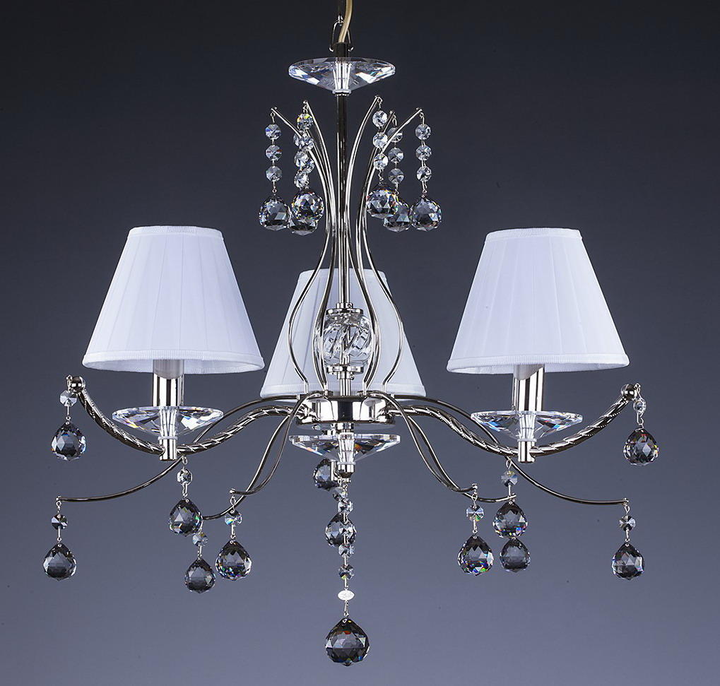 Lustre trois bras avec abat-jours blancs et pendentifs en cristal sur fond gris.