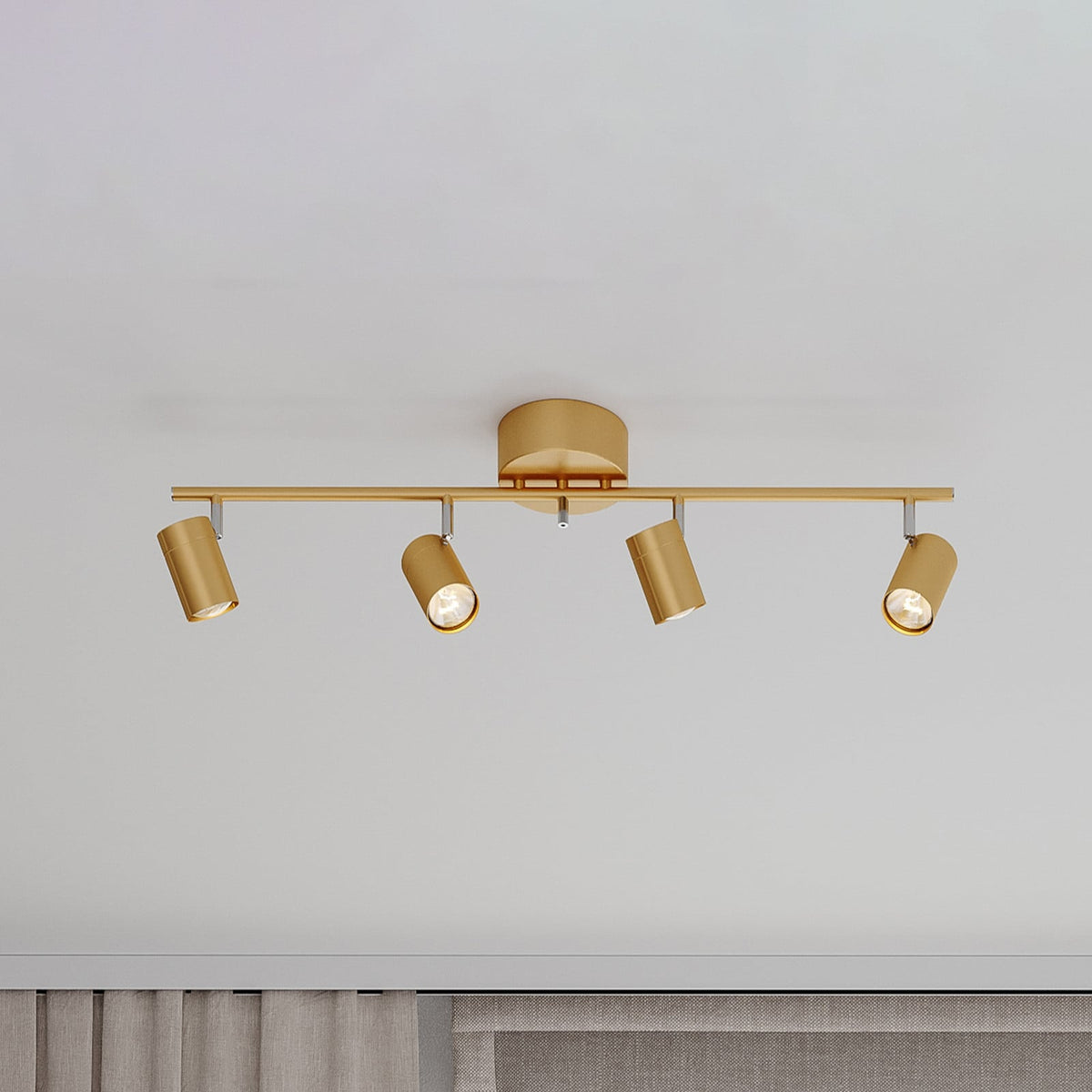 Vue de face du spot doré à quatre têtes cylindriques orientables, fixé au plafond.
