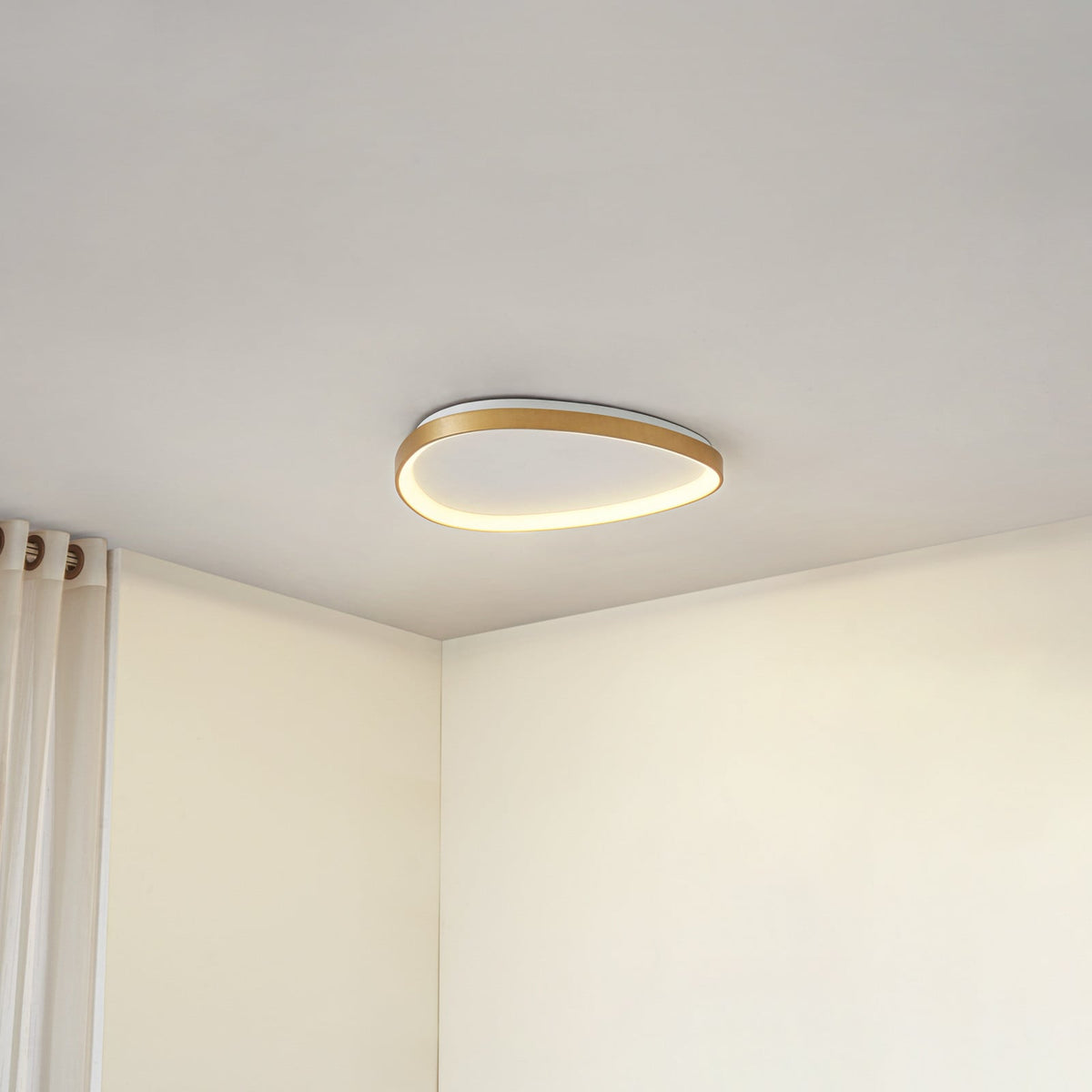 Plafonnier doré allumé au plafond, avec un rideau blanc visible sur la gauche.