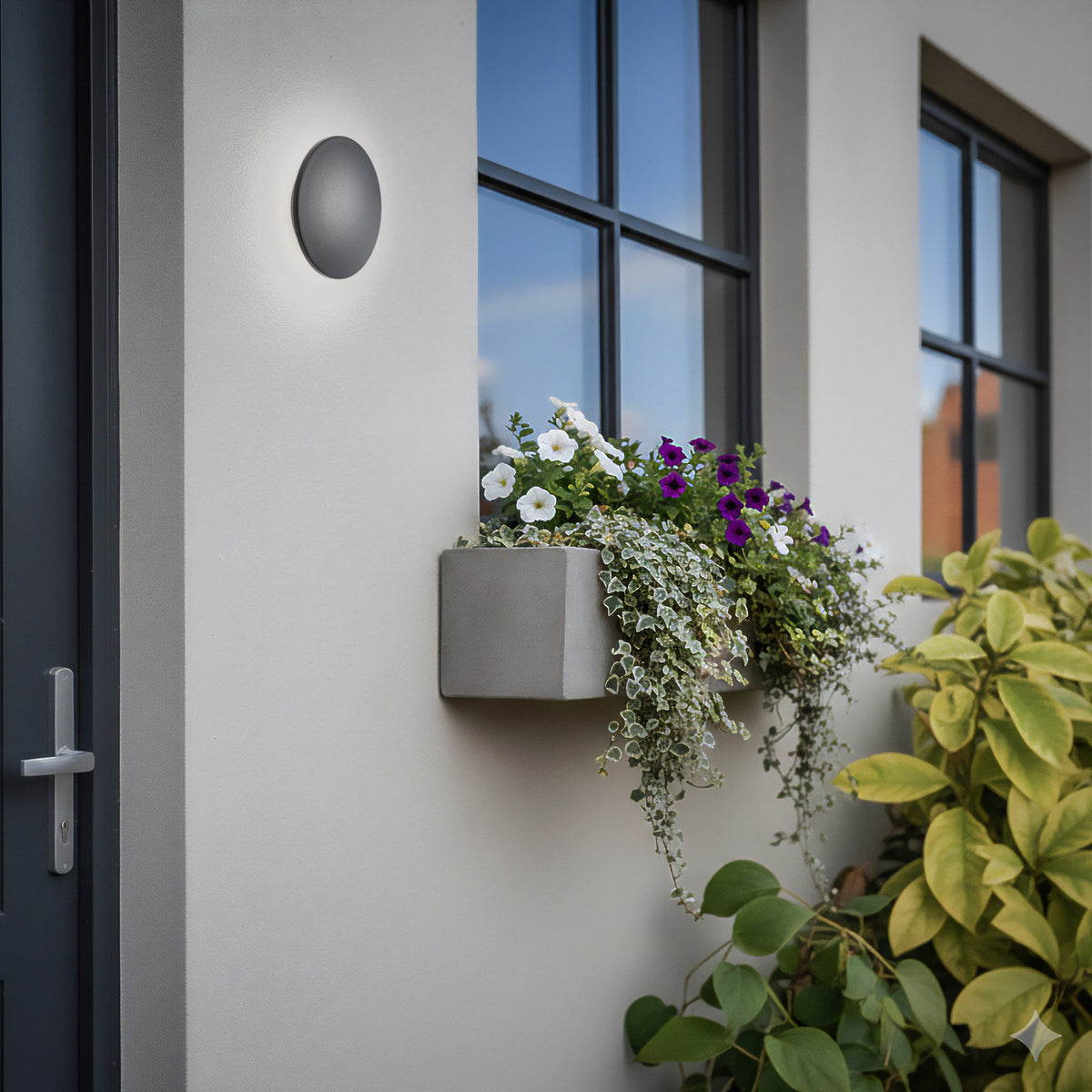 Luminaire mural noir installé près d'une porte vitrée, avec jardinière fleurie.
