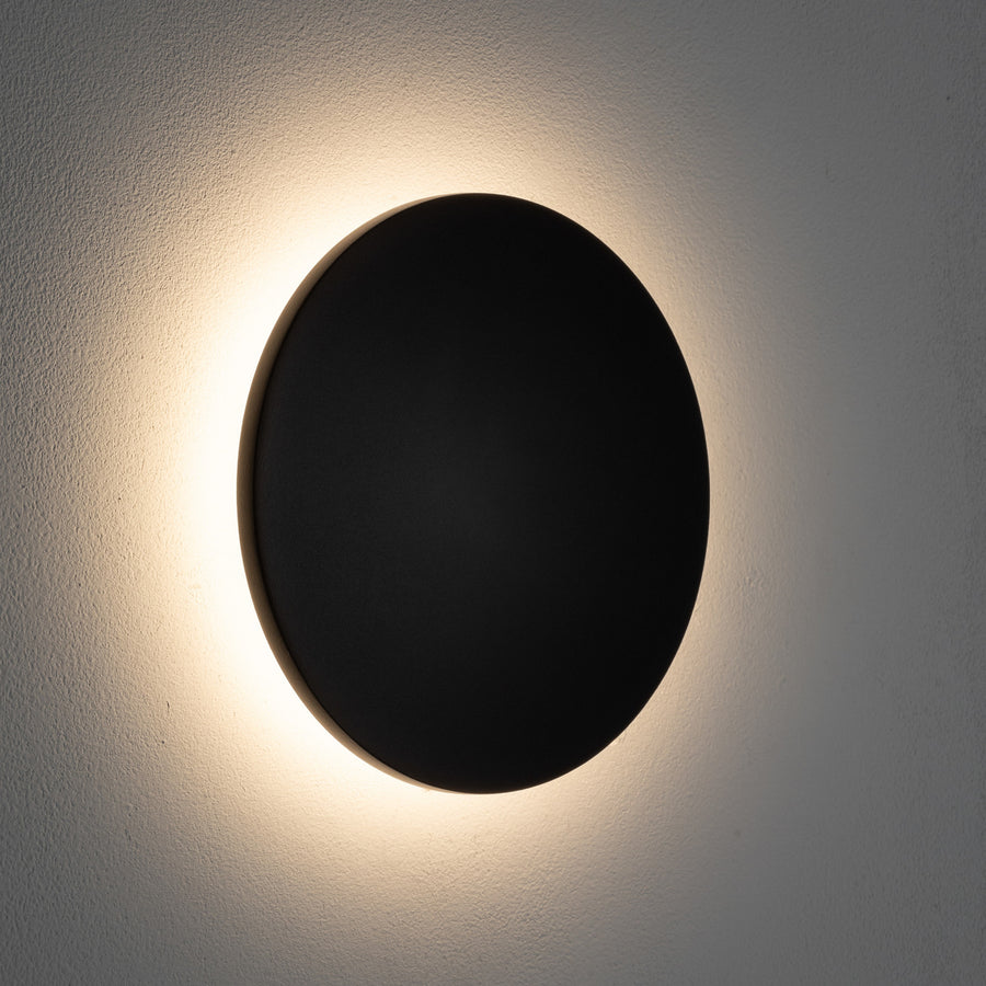 Applique allumée projetant un halo de lumière chaude sur le mur.