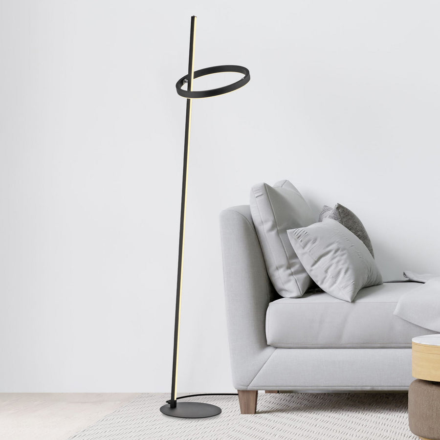Lampadaire à anneau et tige LED noire devant un canapé gris clair.