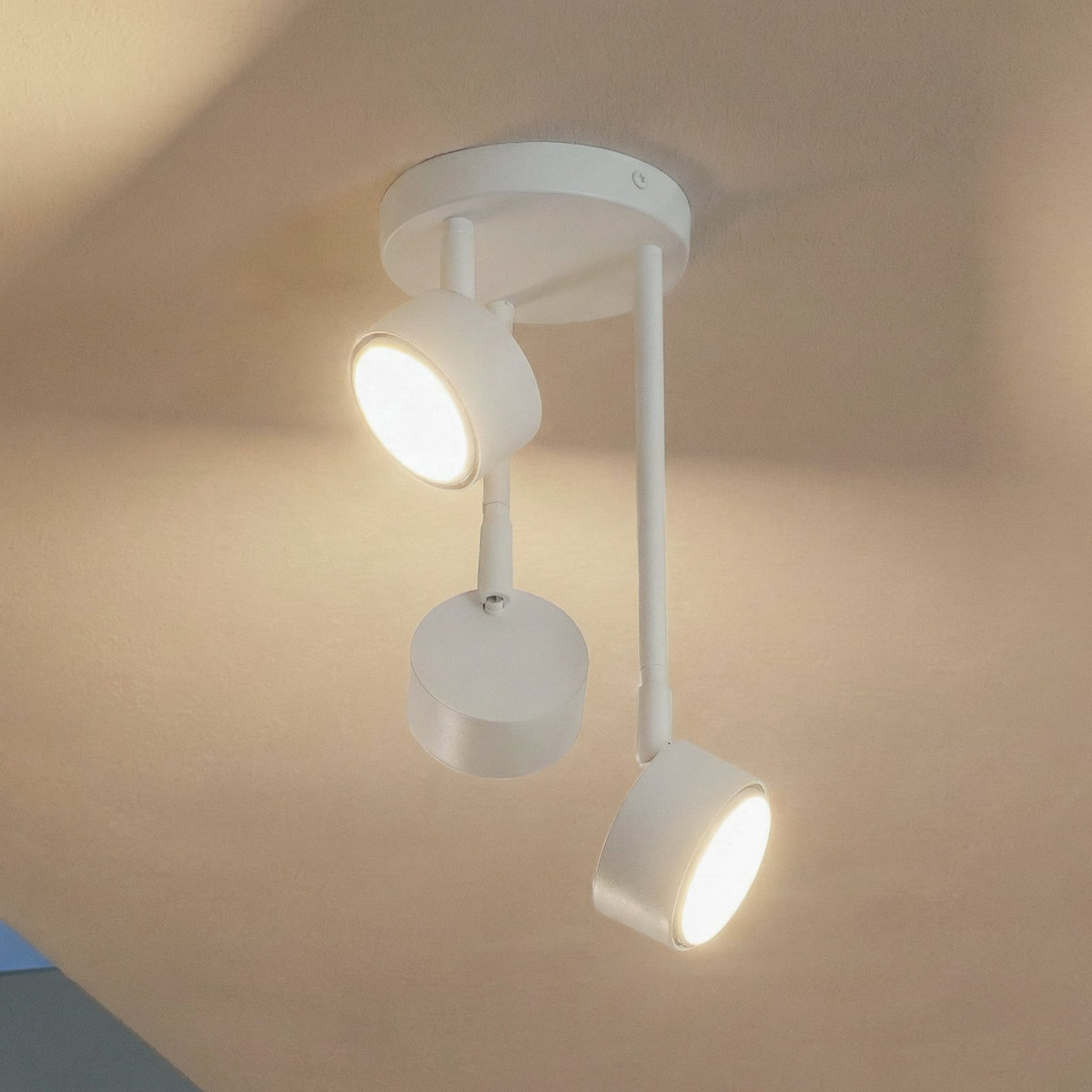Vue rapprochée du spot blanc à trois têtes orientables, une lumière allumée.