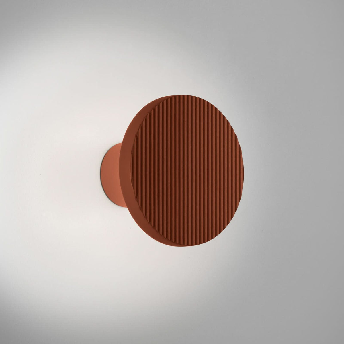 Applique murale terracotta fixée sur un mur clair, lumière douce diffusée autour du disque strié.