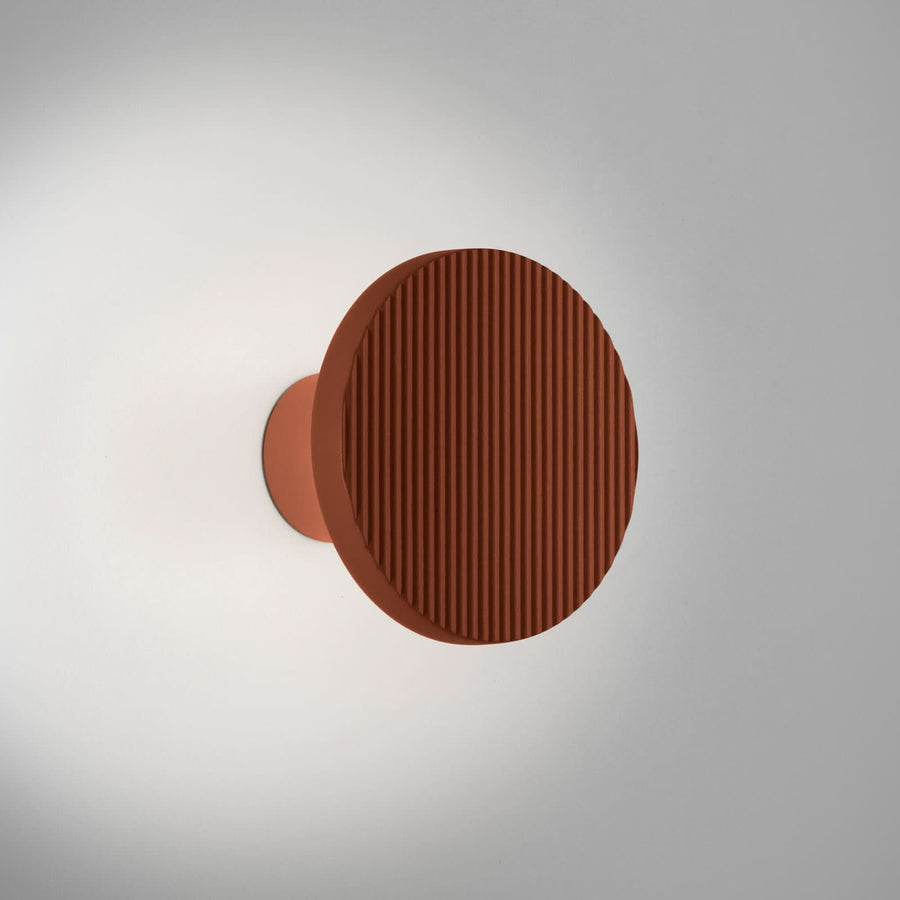 Applique murale terracotta fixée sur un mur clair, lumière douce diffusée autour du disque strié.
