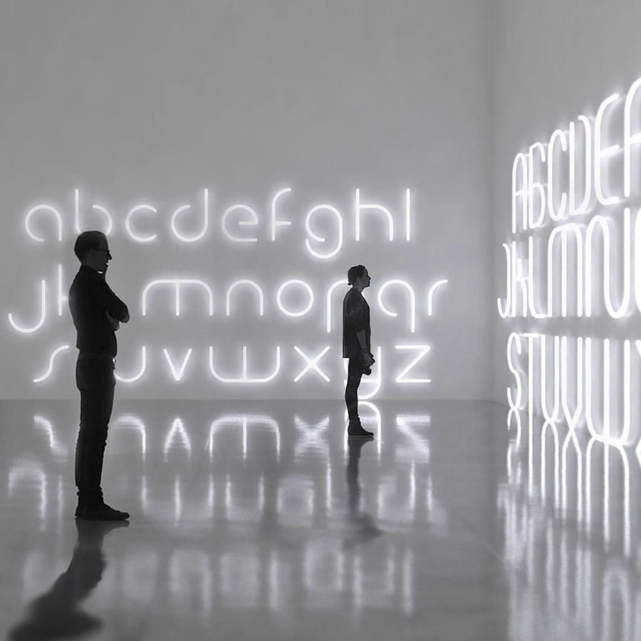 Deux personnes observant une grande installation murale de lettres lumineuses.