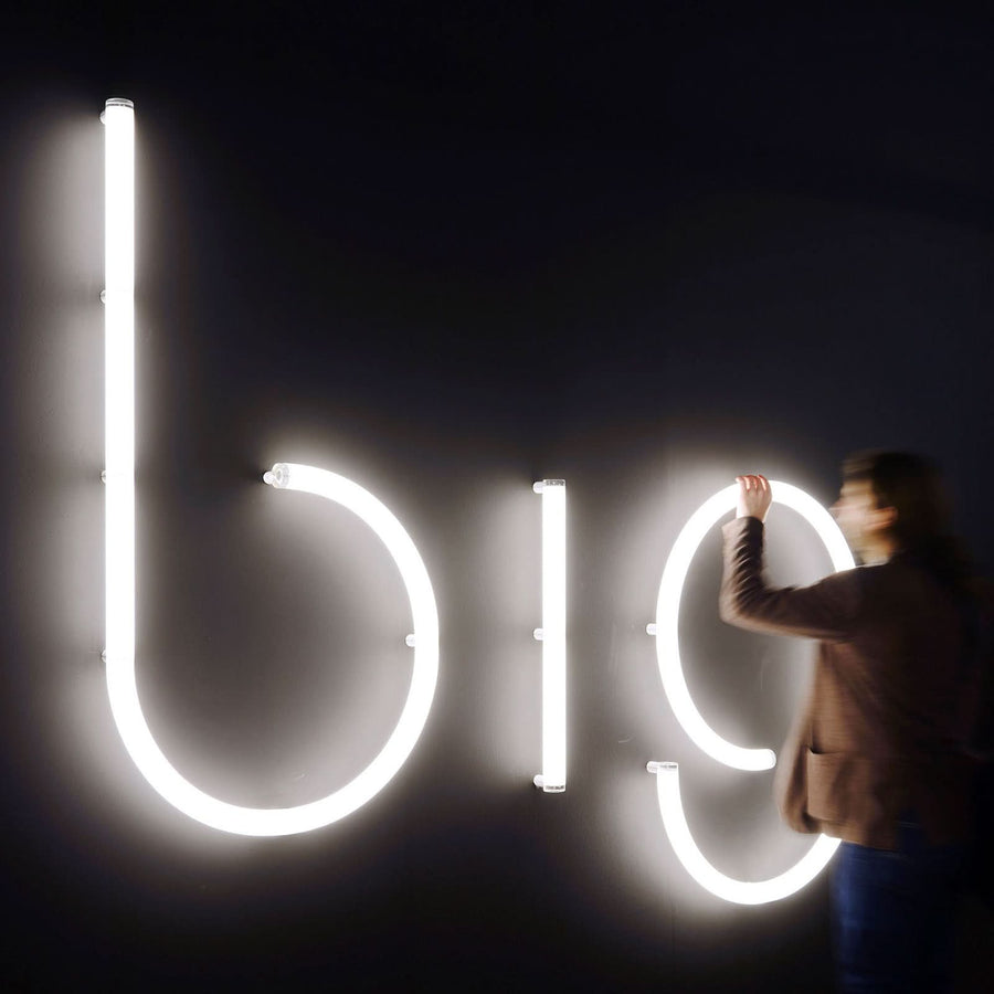 Une personne ajuste de grandes lettres lumineuses blanches sur un mur sombre