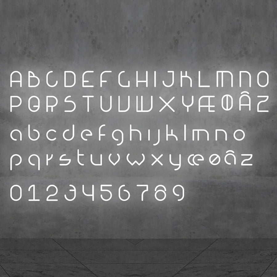 Alphabet complet en lettres blanches lumineuses sur un mur gris.