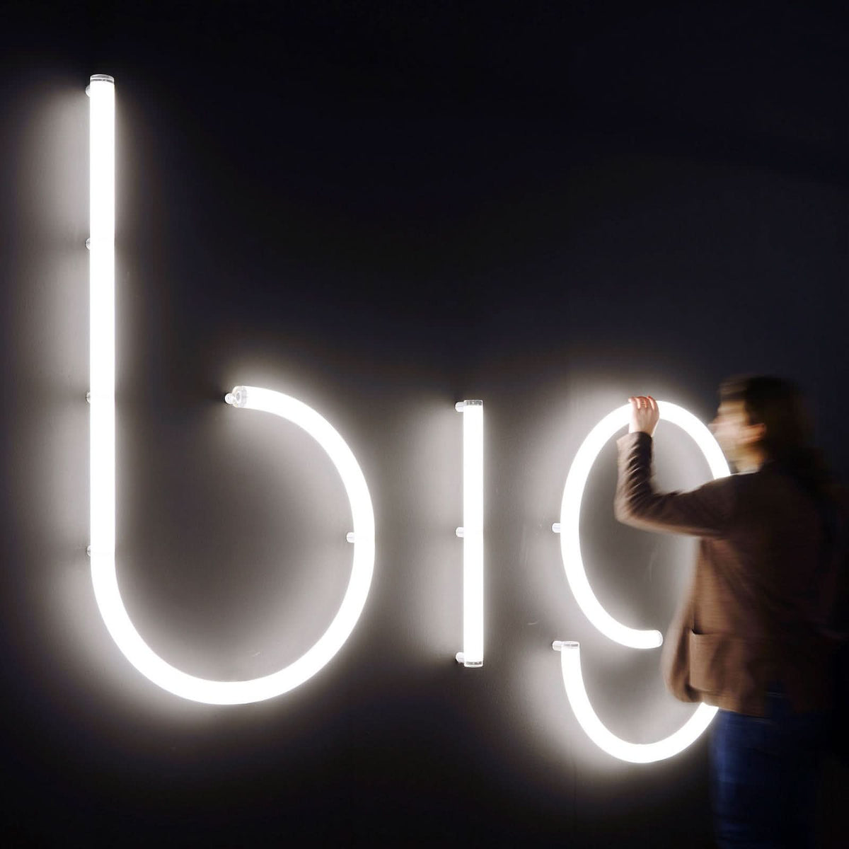 Personne ajustant des lettres lumineuses blanches sur un mur noir.