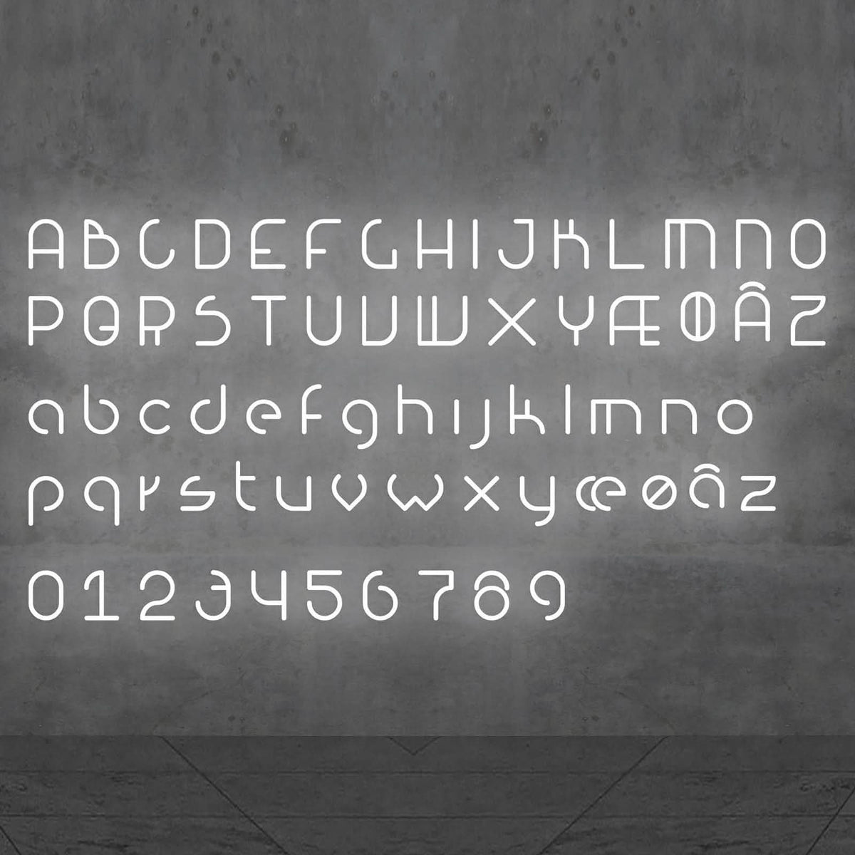 Alphabet complet lumineux, majuscules, minuscules et chiffres, présenté sur un mur béton.