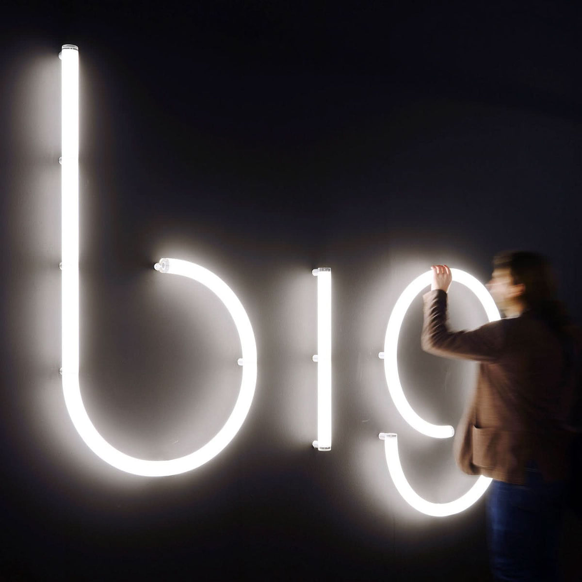 Personne installant une grande enseigne lumineuse à lettres blanches sur un mur sombre