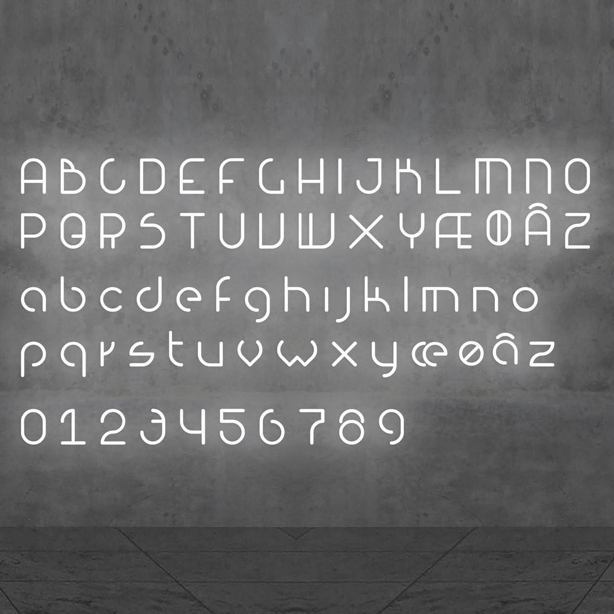Alphabet complet en lettres lumineuses blanches, majuscules, minuscules et chiffres sur béton gris.