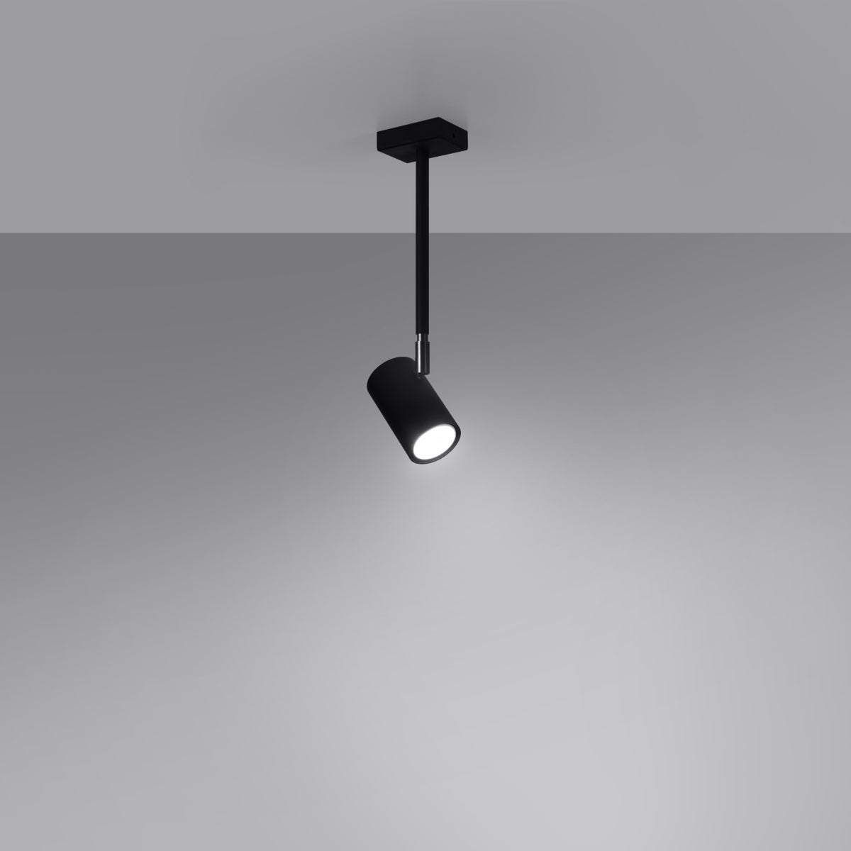 Plafonnier noir allumé fixé au plafond, projecteur incliné vers le bas.