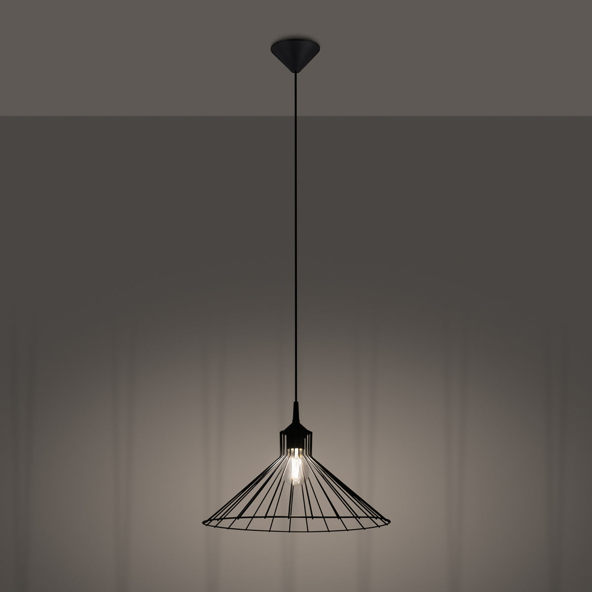Lampe suspendue allumée dans une pièce sombre, éclairant le mur derrière elle.