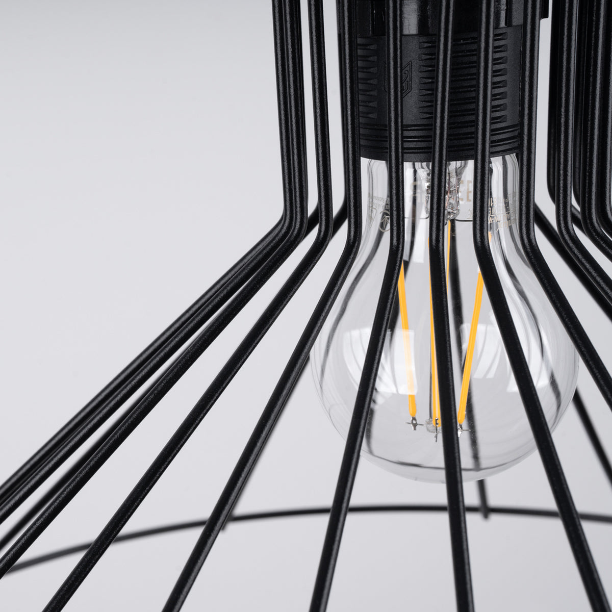 Gros plan sur l’ampoule à filament et la finition noire de la cage métallique.