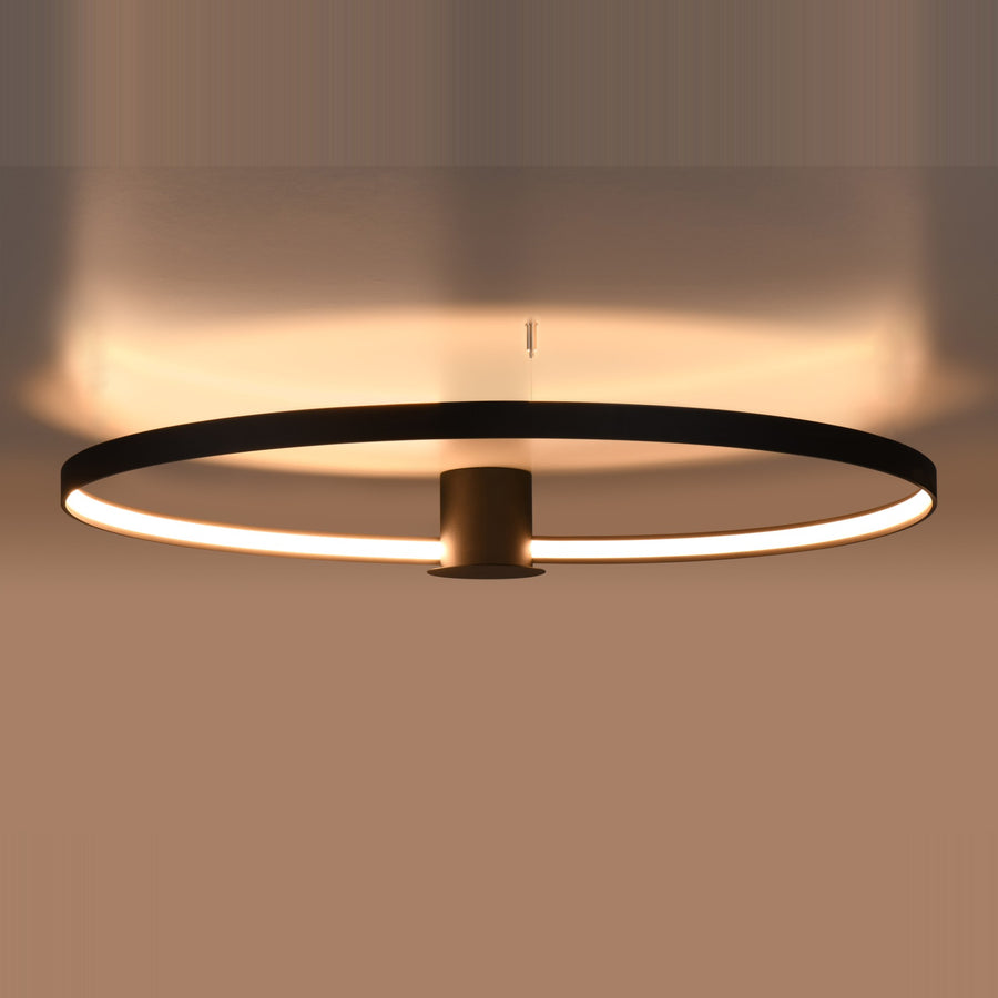 Anneau noir allumé en lumière chaude, halo diffus projeté sur le plafond