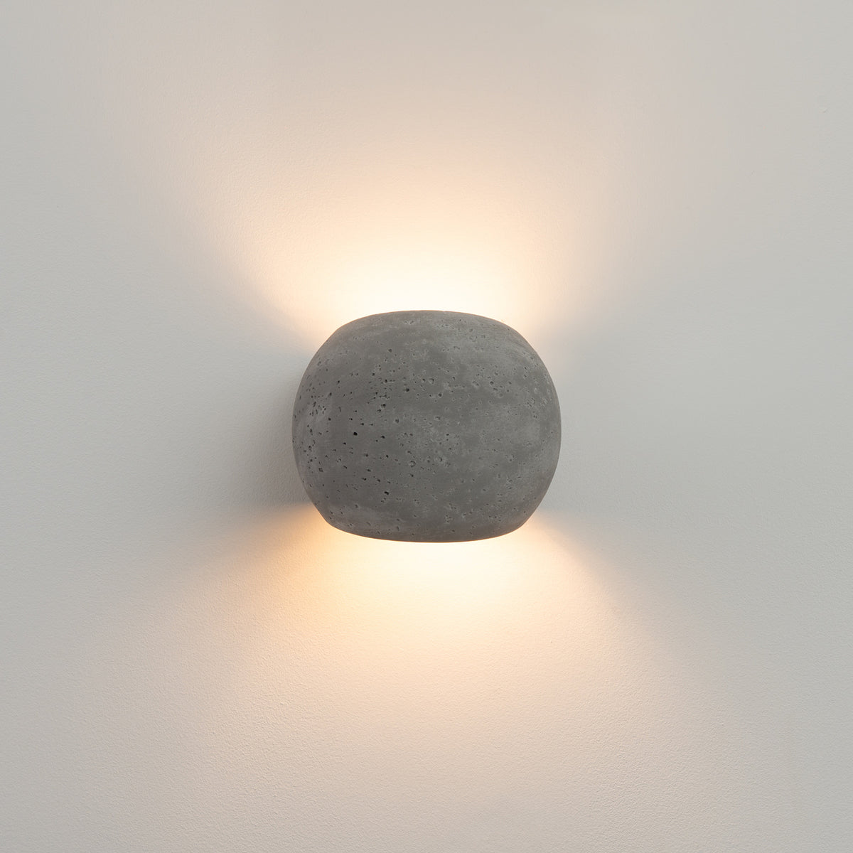 Applique murale en béton allumée, halo lumineux sur mur blanc