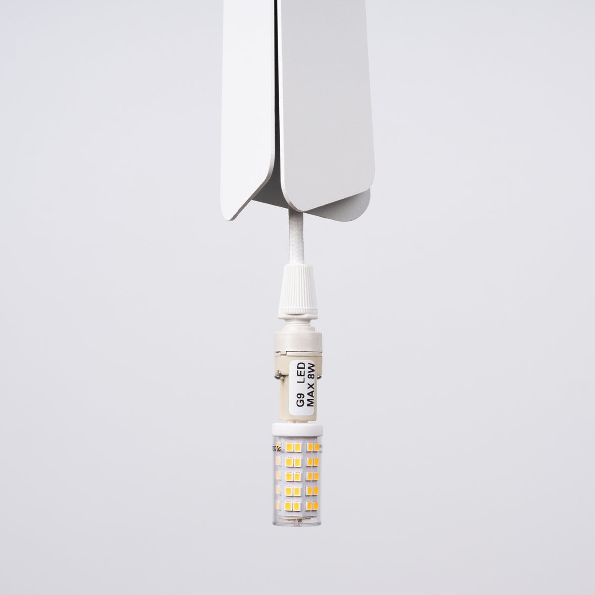 Gros plan sur l'ampoule LED G9 installée dans la douille sous l'abat-jour blanc.