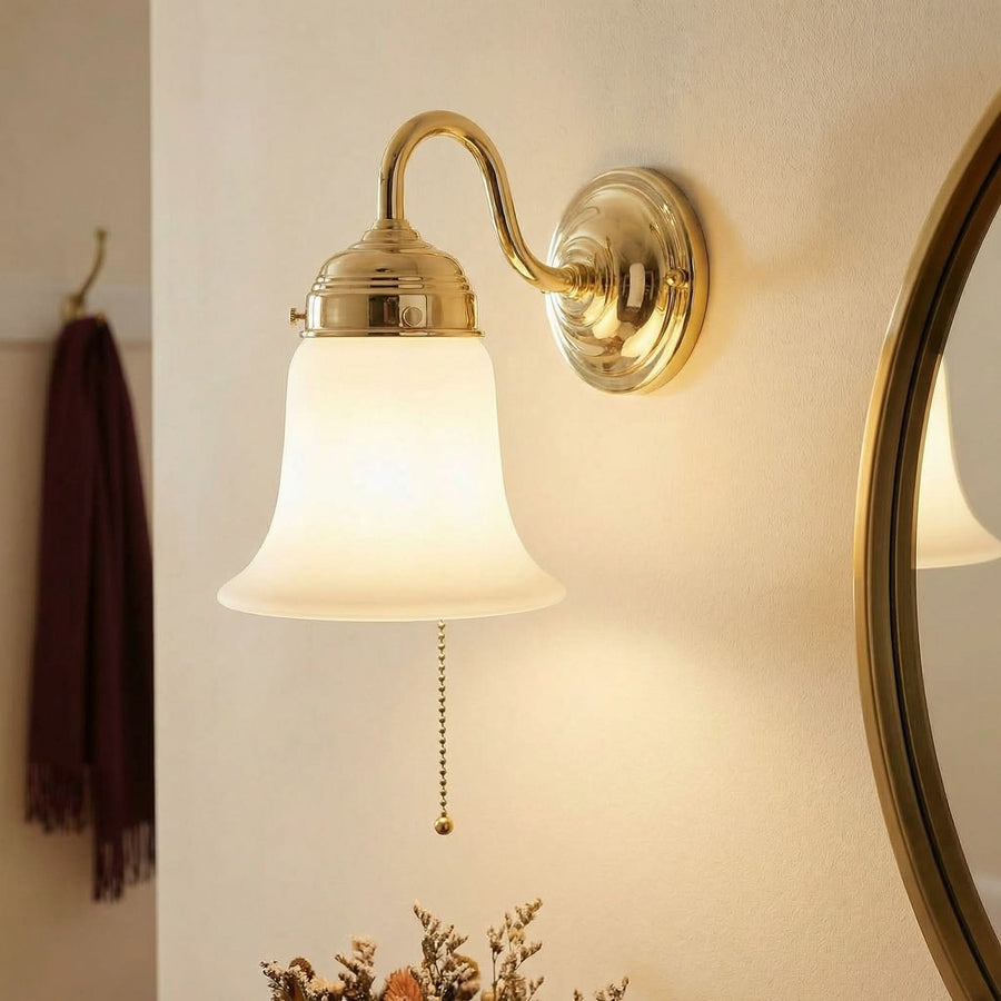 Applique en laiton allumée près d’un miroir rond dans une salle de bain beige.