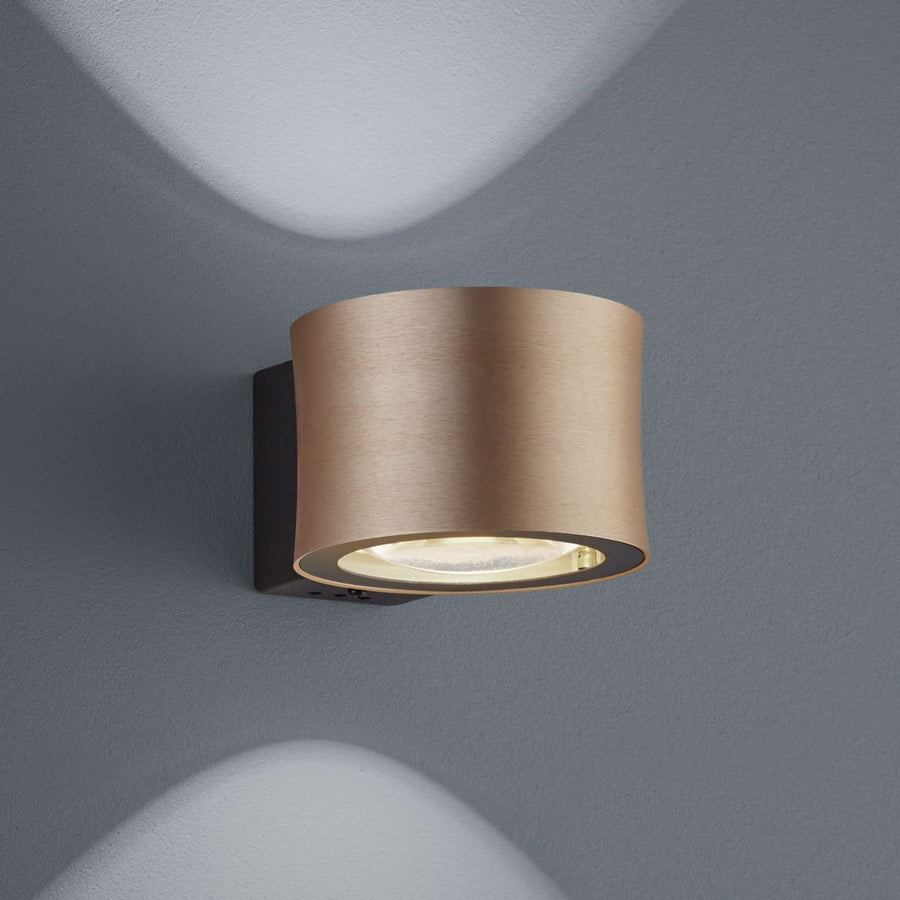 Applique murale cylindrique rosée fixée au mur gris, halo de lumière projeté.