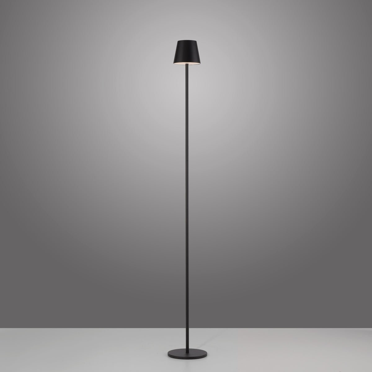 Lampadaire noir allumé sur fond gris, halo de lumière douce autour de l'abat-jour.