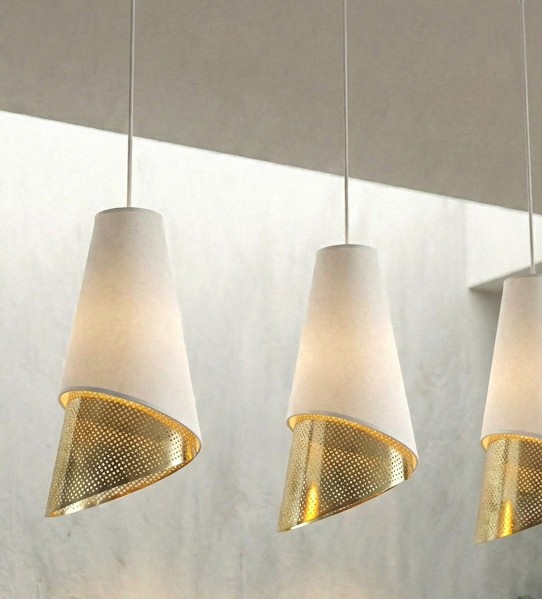 Détail en contre-plongée des abat-jours tissés et cônes dorés perforés