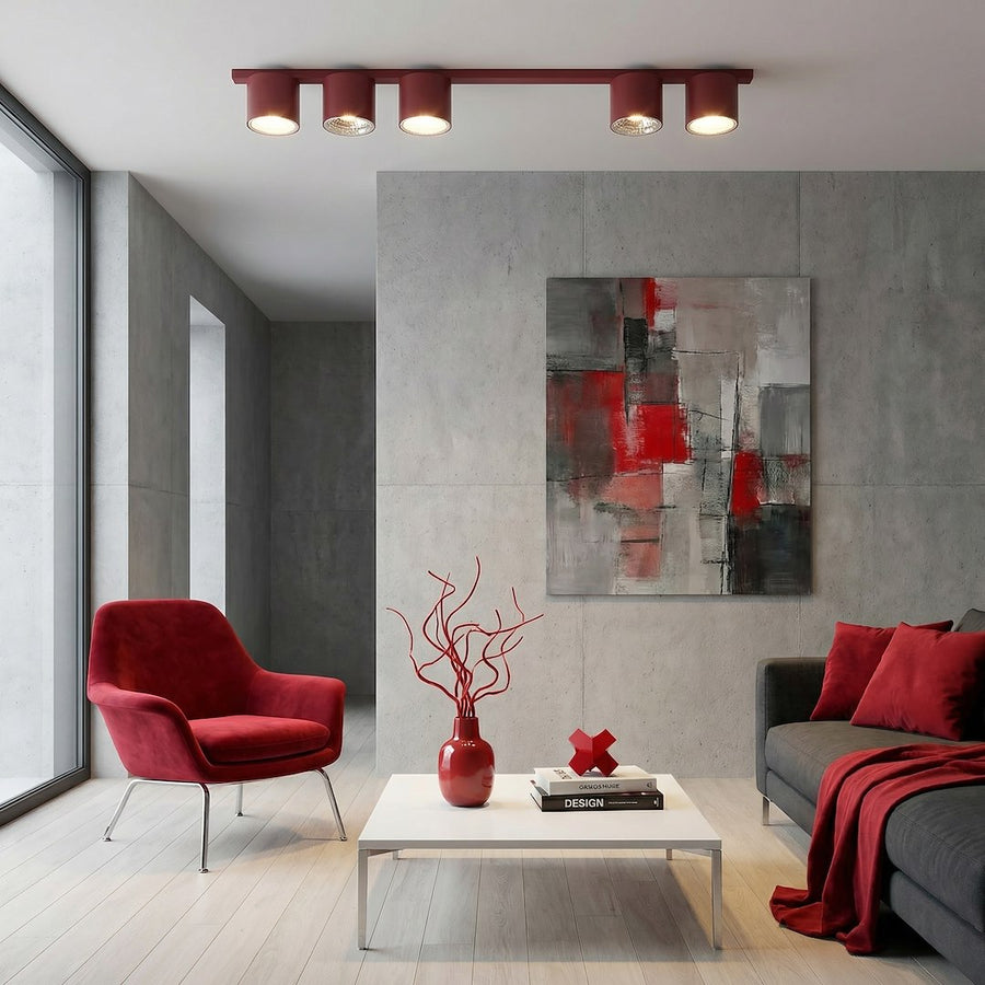 Mise en ambiance intérieure béton brut avec fauteuil bordeaux et décoration rouge.