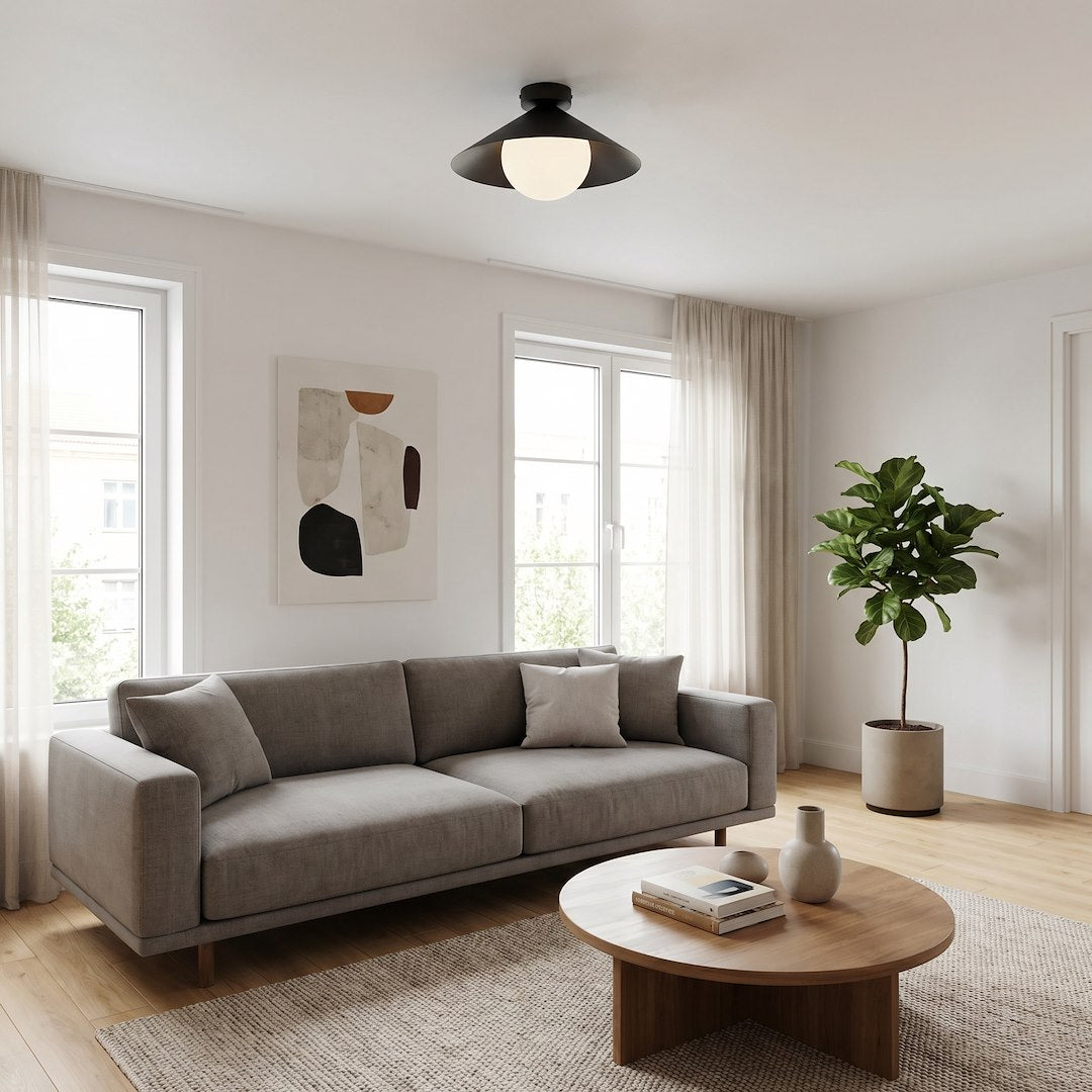 Mise en ambiance salon clair, plafonnier noir allumé au-dessus du canapé gris.