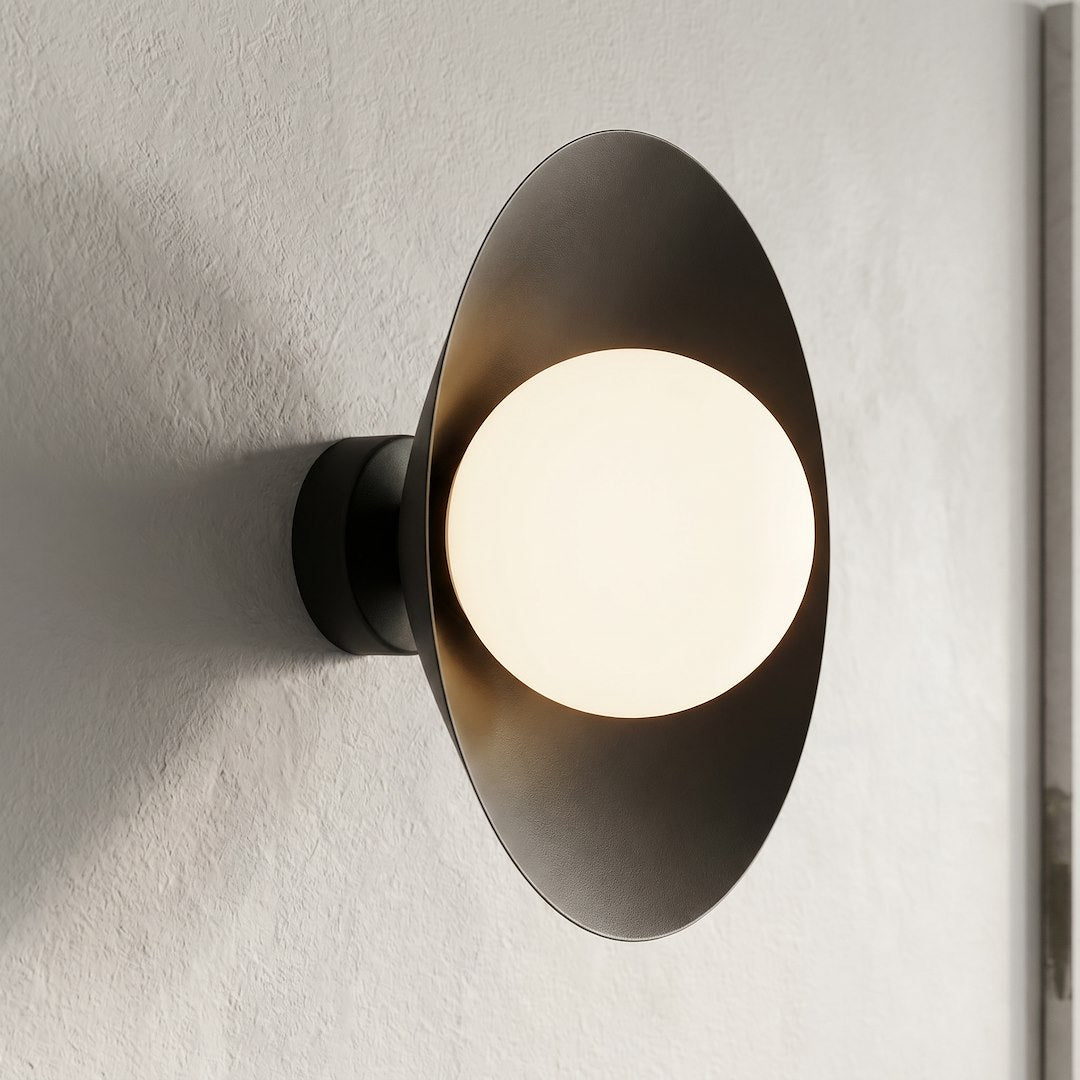 Gros plan sur mur texturé, applique murale noire allumée et diffuseur en verre blanc lumineux.