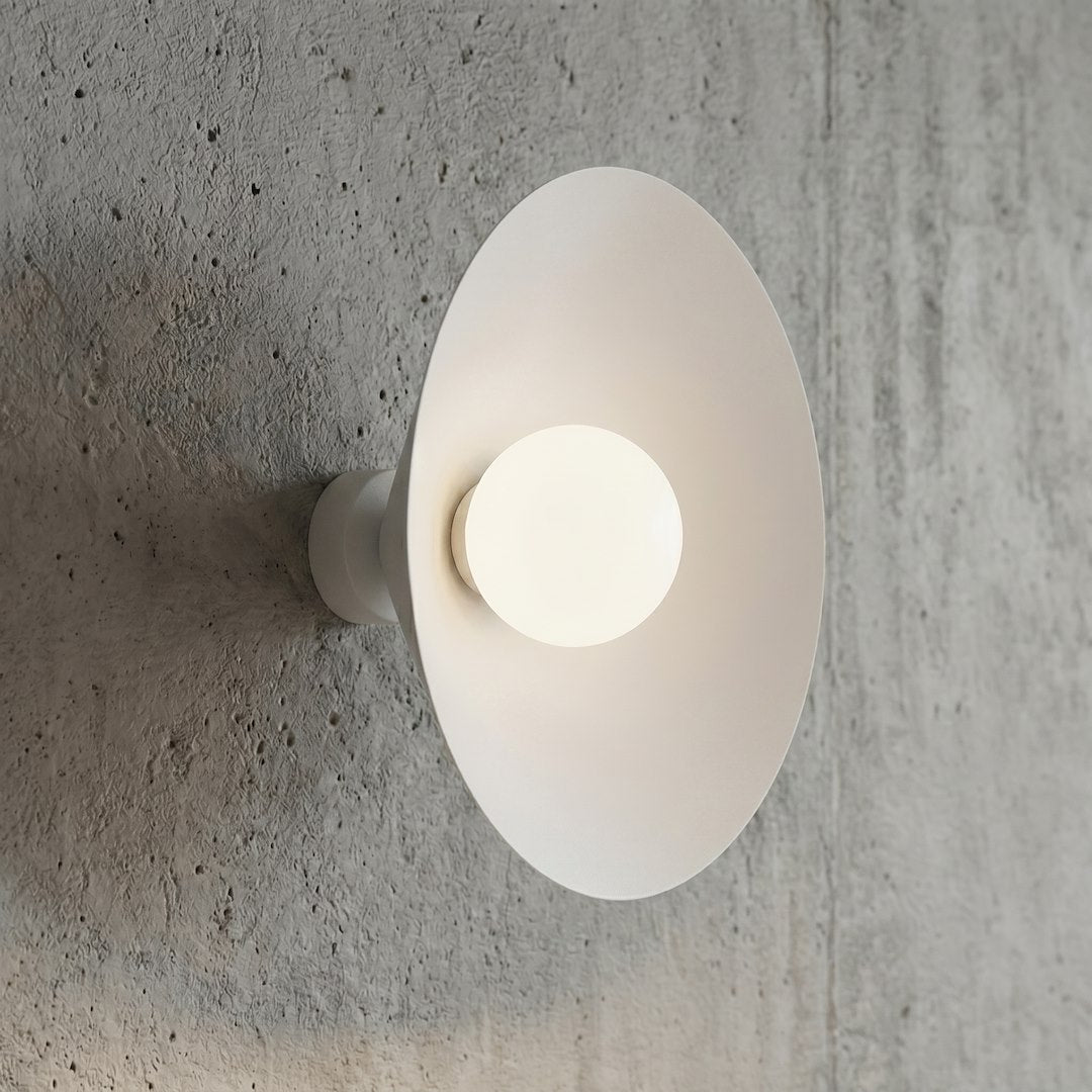 Détail de l'applique allumée sur un mur béton texturé, disque et sphère lumineuse