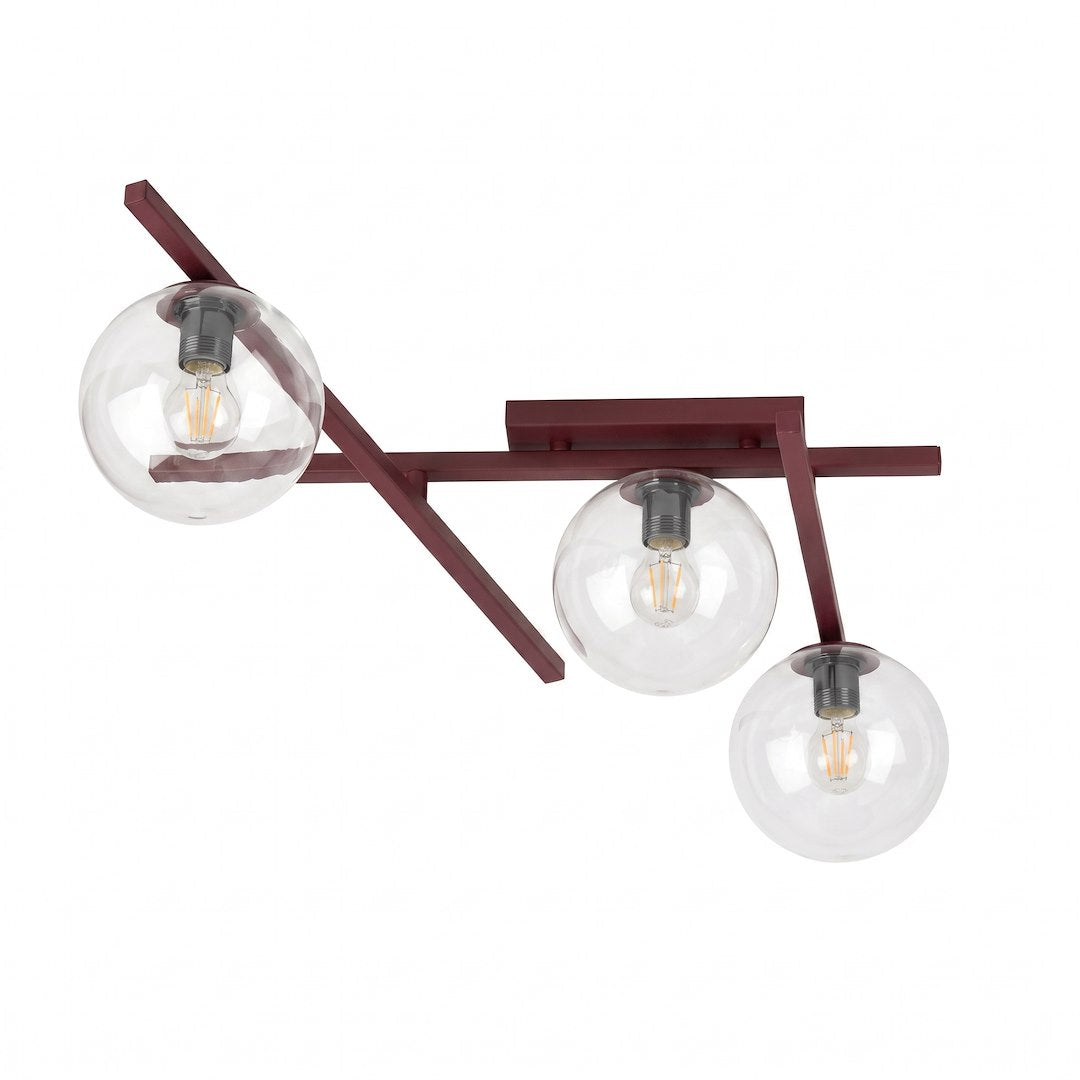 Plafonnier trois globes en verre transparent montés sur bras métalliques croisés bordeaux, fond blanc.