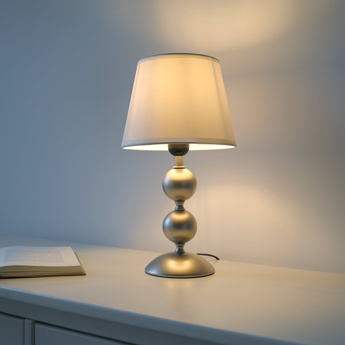Mise en ambiance nocturne sur un meuble blanc, lumière chaude et livre ouvert