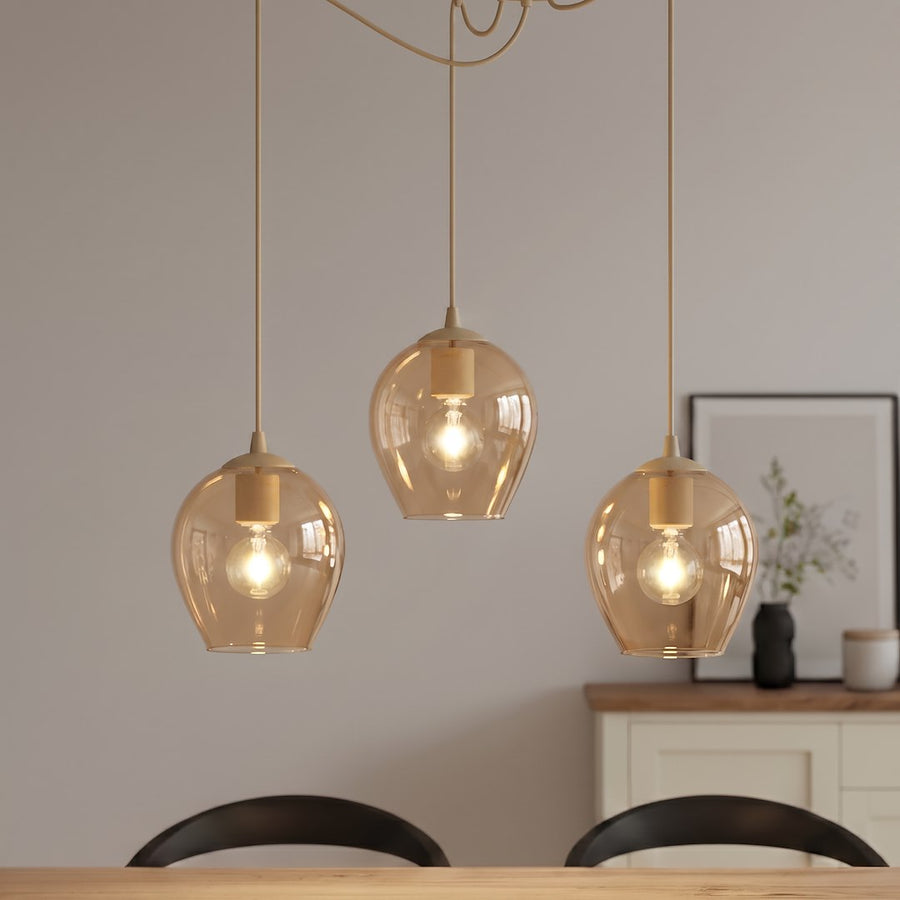 Gros plan des trois globes en verre ambré éclairés, suspendus devant un buffet clair