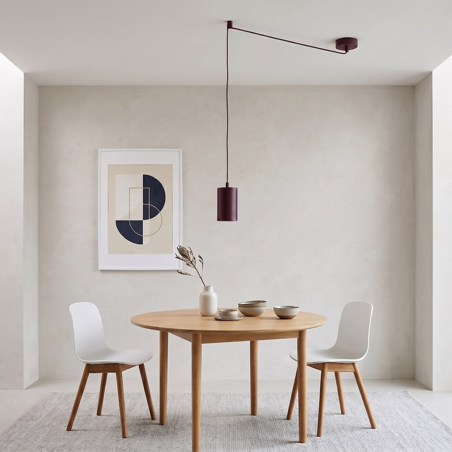 Mise en scène salle à manger : luminaire bordeaux suspendu au-dessus d'une table ronde en bois
