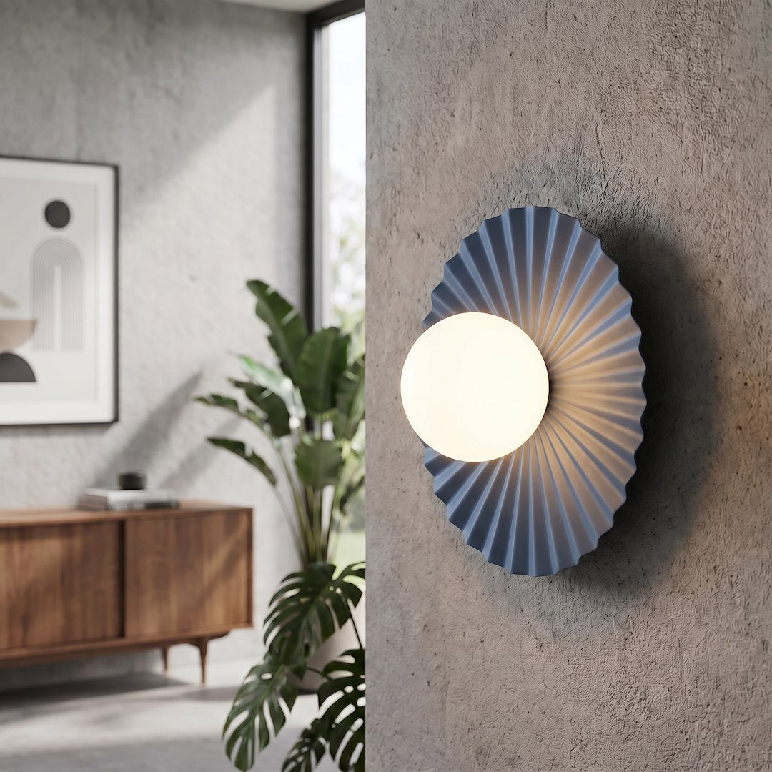 Luminaire fixé sur un mur béton gris, près d'une plante verte et d'un meuble