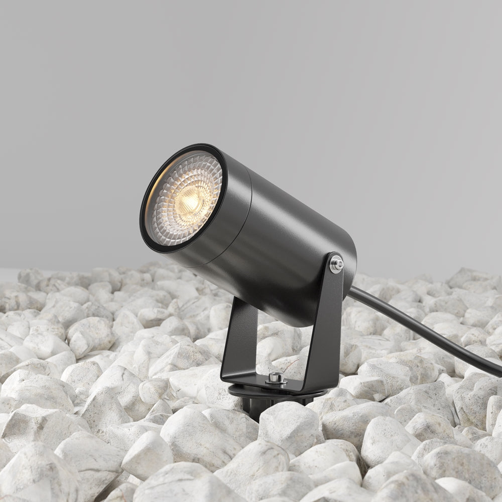 Projecteur cylindrique noir orientable sur piquet, installé parmi des galets blancs