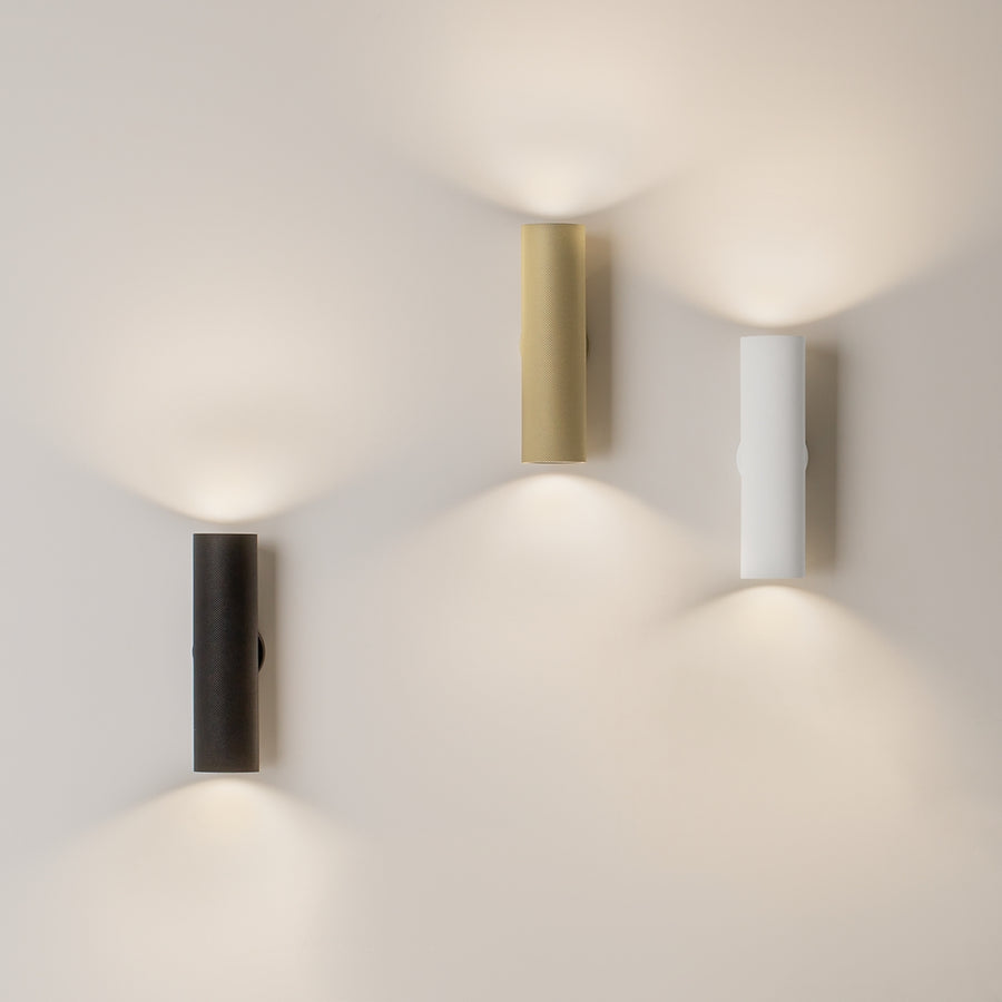 Mise en ambiance avec trois appliques déclinées en noir, laiton et blanc sur un mur.