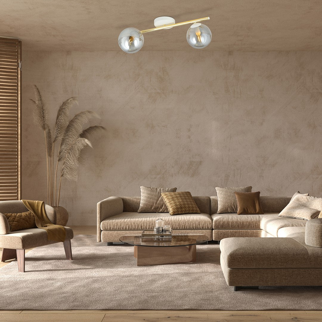 Plafonnier allumé éclairant un salon beige avec canapé d'angle et plantes séchées.