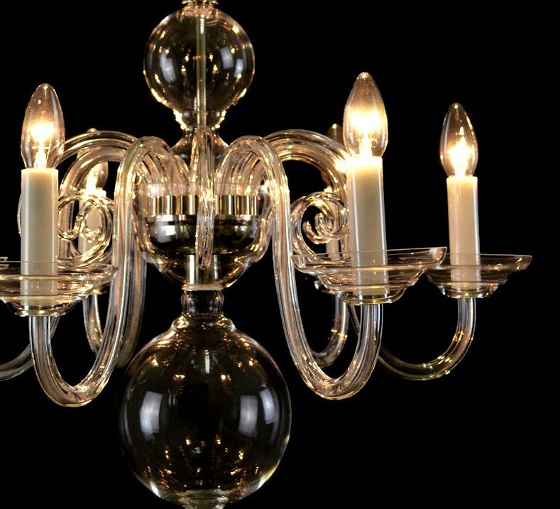 Gros plan du lustre allumé, bougies ivoire et ampoules filament, reflets dorés