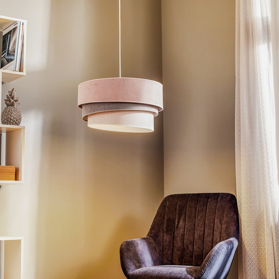 La suspension rose et grise éclaire un coin salon avec fauteuil et étagère.