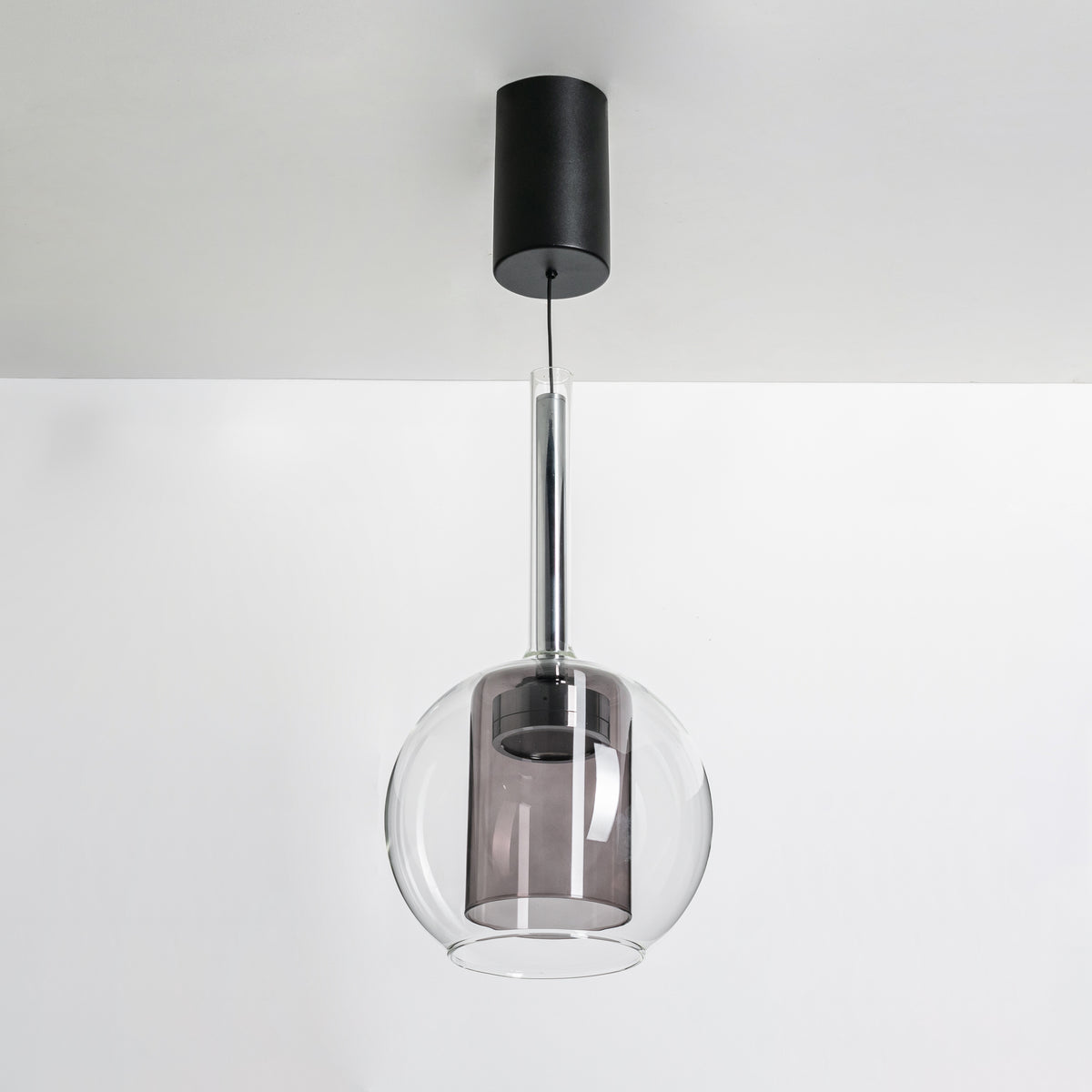 Vue de face de la suspension éteinte, globe de verre fumé sur tige fine.