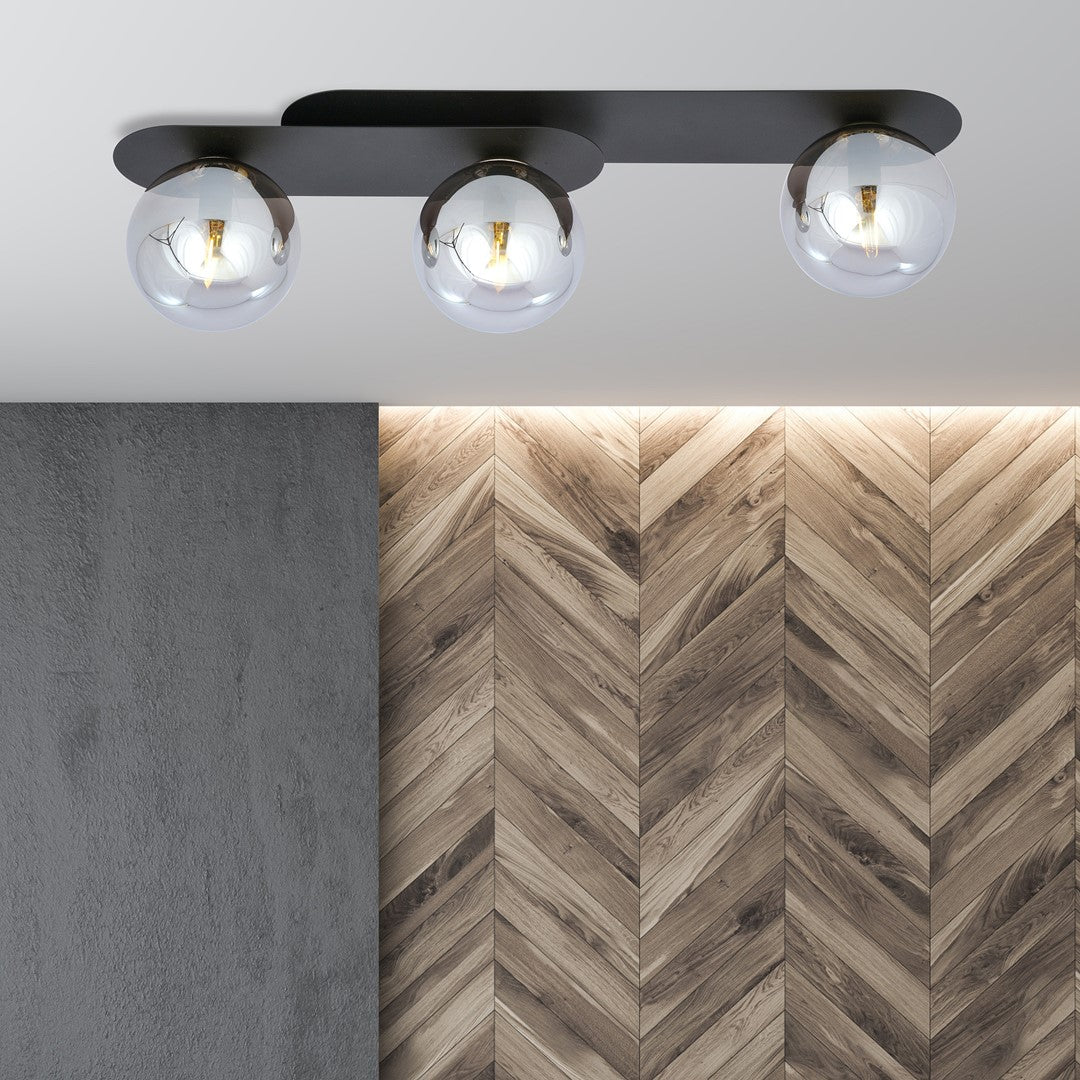 Luminaire allumé fixé au plafond devant un mur en bois en chevrons.
