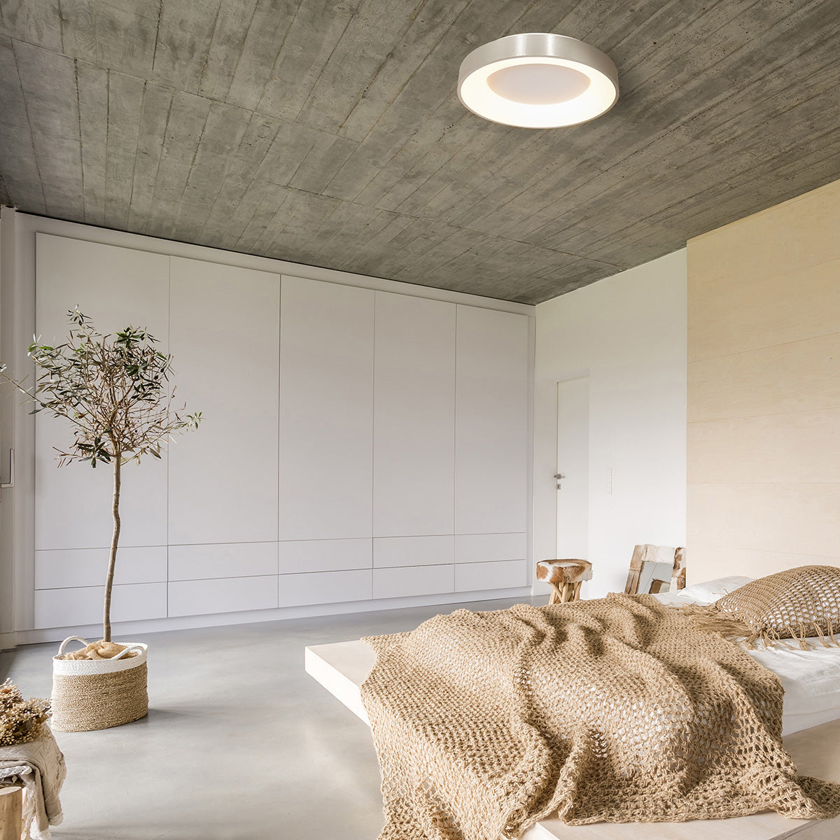 Plafonnier installé au plafond béton d'une chambre lumineuse, décoration naturelle.